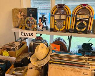 Elvis memorabilia display featuring collectible figures, records, CDs, jukebox-style radios, vintage audio pieces, and music-themed nostalgia items. Great assortment for Elvis fans, record collectors, and buyers looking for retro music and entertainment collectibles.