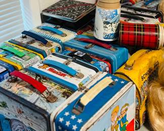 Vintage metal lunch box collection with character, patriotic, school bus, and novelty designs, plus retro thermoses and collectible tins. Great display pieces for collectors of vintage lunch boxes, pop culture memorabilia, and nostalgic childhood items.