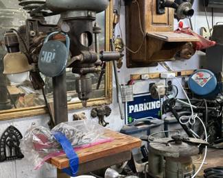 Vintage workshop wall featuring an antique Delta Homecraft drill press, wall-mounted wooden crank telephone, industrial shop tools, old signage, mirror, and garage collectibles. Strong mix of antique tool room pieces, industrial decor, and unusual man-cave display items for collectors, restorers, and pickers.