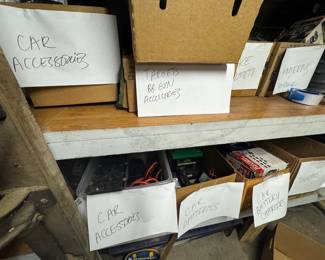 Garage shelf area with sorted boxes of car accessories, car batteries, chargers, thermoses, and target/BB gun accessories. Organized overflow storage with useful garage lots, automotive items, and picker-friendly shelf inventory.