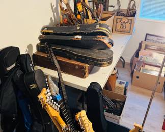 Music room and instrument collection featuring guitars, mandolins, violins, brass horns, cases, and framed artwork. Great assortment of string instruments, band pieces, and musical accessories for players, collectors, and resellers.