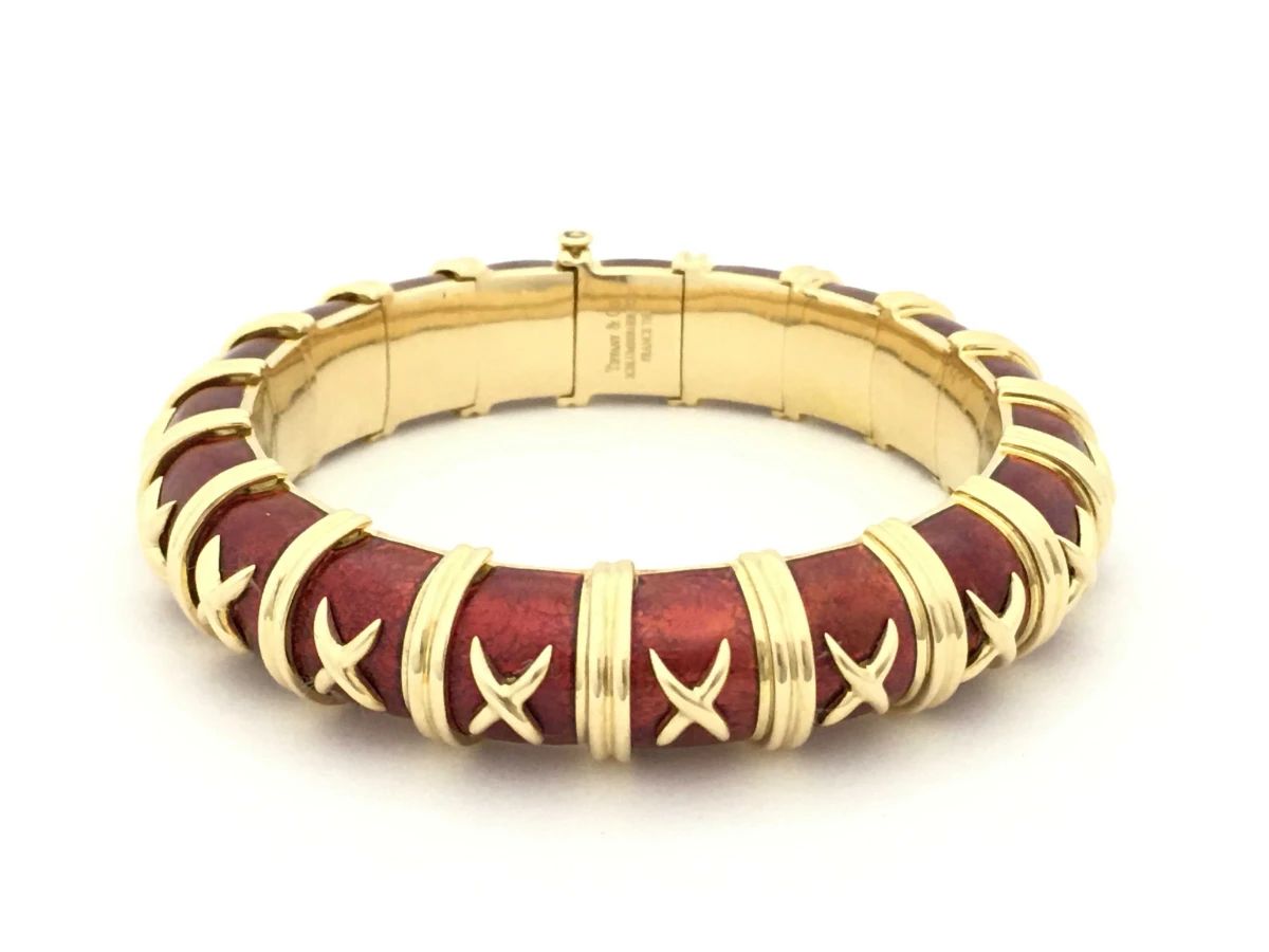 Striking Tiffany & Co. bracelet designed by Jean Schlumberger, crafted in solid 18K yellow gold with rich red enamel panels. The iconic Croisillon design features repeating gold cross motifs over the enamel, a signature element of Schlumberger’s imaginative and sculptural jewelry style. Bold and highly recognizable, this bracelet reflects the distinctive craftsmanship and artistic vision associated with Tiffany & Co.’s most celebrated designer.