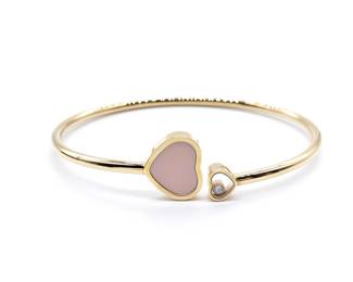 Iconic Chopard Happy Heart bracelet crafted in solid 18K rose gold, featuring a soft pink opal heart motif accented by a single floating diamond enclosed within sapphire crystal. The elegant open heart design highlights Chopard’s celebrated Happy Diamonds concept, combining refined materials with playful movement and timeless femininity. A recognizable and highly sought after piece from one of Chopard’s most beloved collections.