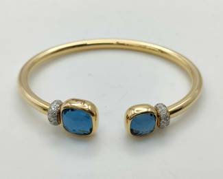 Description: Elegant Pomellato Nudo cuff bracelet featuring two cushion-cut blue topaz gemstones set in polished 18K yellow gold with diamond pavé accents. The iconic open cuff design highlights Pomellato’s signature minimalist Italian style and vibrant gemstone color. A refined and recognizable piece from the celebrated Nudo collection.
