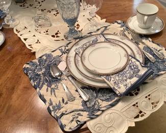 The place setting if China with napkins, crystal glasses and blue glasses.