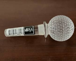 Mikasa "Tee Time" Crystal Golf Ball Bottle Stopper. It is a functional bar accessory designed to preserve wine or liquor by creating an airtight seal with its silicone or plastic band