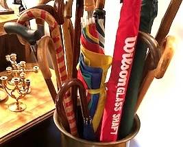 Brass umbrella stand with antique wooden canes and umbrellas.