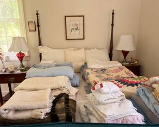 Four poster bed piled with vintage quilts blankets and linens