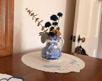 Blue Willow transferware pitcher with floral arrangement and embroidered doily