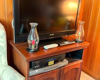 Flatscreen TV on cherry media cabinet with hurricane glass candle holders