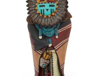 1204 Gerry Quotskuyva (b. 1959, Hopi-Tewa) A painted carved cottonwood 'Sunface' katsina, 2012 With incised signature, date, and title to underside: Quotskuyva / '12 [Tawa], depicted with feathers centering the face, wrapped in a wearing blanket 12.375" H x 5.75" W x 4.75" D Estimate: $300 - $500