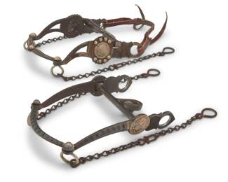 1107 Two Les Vogt mixed metal parade style horse bits Late 20th/21st century Each stamped: Les Vogt's / Flat Creek / [Model no] Comprising two ornate bits in mixed metal and sterling silver, one with extensive chased sterling silver overlay, rosettes, and silver button accents (No. 2397-3; 9.5" H x 6.5" W) and one with sterling silver rosettes and bands of sterling overlay to sides and front (No. 2343-3; 9.25" H x 6" W), each with chain extenders, and one with a hide leather nose band 2 pieces Estimate: $300 - $500