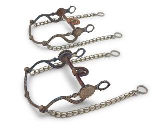 1106 Two Edwin George E.G. Field mixed metal parade style horse bits Early 21st century; Santa Barbara, California Each stamped: E.G. Field / [date] Comprising two mixed metal 'half breed' bits each with deep striped chasing and applied sterling silver rosettes and buttons, one with copper details (2005; 8.5" H x 6.125" W) and one with purple and blue metallic finish details (2007; 8.75" H x 6.125" W), each with chain extensions 2 pieces Estimate: $1,000 - $1,500