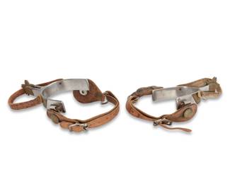 1108 A pair of Crockett Western spurs 20th century Each stamped: Crockett / Stainless The stainless steel spurs with small five point star rowels and inset chased brass metal accents, each with two leather straps 2 pieces Each: inner heel band: 3.25" W ; heel depth: 3" D; shank: 1.875" L; rowels: 1.5" Dia. Estimate: $300 - $400