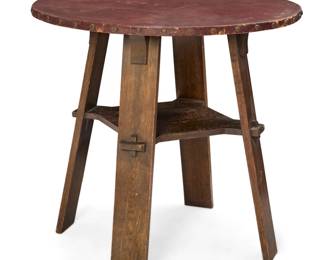 1294 An Arts & Crafts leather top table Early 20th century Unmarked In the style of Gustav Stickley, the top clad in oxblood leather with metal tacking, over four corbeled legs and an underteir with keyed tenon joinery 29.25" H x 31" Dia. Estimate: $800 - $1,200