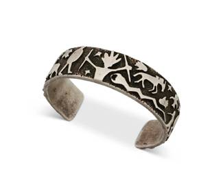 1343 A Danny Romero sterling silver cuff bracelet Danny Romero (1954-2018; Yaqui/Spanish) Stamped: D R.MER. / FINE / [pictograph] A chunky sterling silver cuff with figural silver overlay featuring various Pueblo and Southwest motifs 7.25" total inner C x 0.75" H, gap: 1.5" 90.0 grams Estimate: $500 - $700