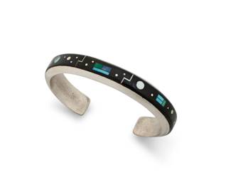 1348 An Albert Yazzie Navajo sterling silver and channel set inlay cuff bracelet Albert Yazzie (b.1954, Diné) Stamped: AY / Sterling A narrow cuff with delicate multistage silver, turquoise, lapis lazuli, mother of pearl, spiny oyster, and black stone channel and mosaic inlay, with various sized dot, arrow and celestial motifs 7.125 total inner C x 0.5" H, gap: 1.125" 43.9 grams gross Estimate: $500 - $700
