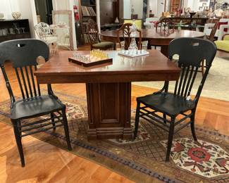 eatures a heavy mahogany pedestal games table with a robust architectural base, paired with two vintage ebonized spindle-back chairs. The chairs feature "ox-yoke" top rails with integrated handles and a charming, factory-distressed finish. A perfect blend of traditional weight and rustic contrast.