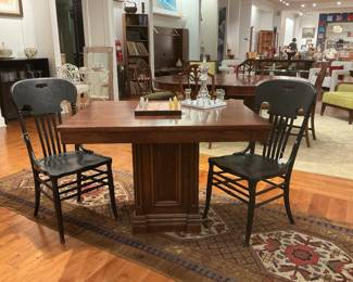 eatures a heavy mahogany pedestal games table with a robust architectural base, paired with two vintage ebonized spindle-back chairs. The chairs feature "ox-yoke" top rails with integrated handles and a charming, factory-distressed finish. A perfect blend of traditional weight and rustic contrast.