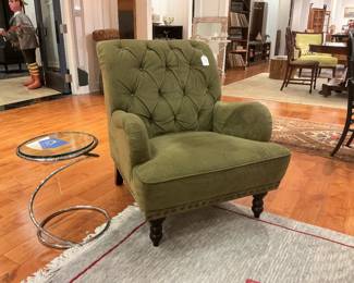 Elegant seating pairing featuring a classic tufted armchair in sage green velvet with brass nailhead trim and turned espresso legs. Paired with a contemporary minimalist side table featuring a circular glass top and a sculptural chrome spiral base. 