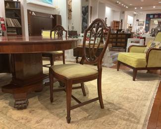 Elegant set of five vintage mahogany-finished dining chairs featuring classic Hepplewhite shield backs with ornate wheat-ear carvings. The set includes tapered legs with H-stretchers and upholstered seats in a neutral, textured gold-tone fabric. 