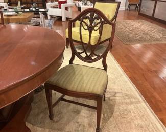 Elegant set of five vintage mahogany-finished dining chairs featuring classic Hepplewhite shield backs with ornate wheat-ear carvings. The set includes tapered legs with H-stretchers and upholstered seats in a neutral, textured gold-tone fabric.
