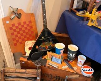 Packed table of antiques, vintage checkerboard, Gulf Oil collectible, guitar, advertising mugs