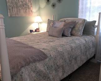white four-poster bed made up with a floral comforter and decorative pillows.