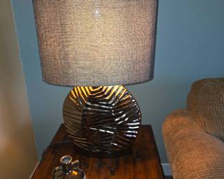 This table lamp features a modern, sculpted ceramic base with a textured, metallic finish and a drum shade. Dive deeper in AI Mode