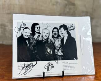 Black-and-white promotional photograph of The Guess Who, measuring 8” H x 10” W. Features five signatures on the front. Includes names of former members and band details at the bottom of the image. Housed in a protective sleeve.