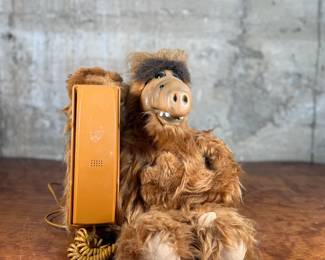 A telephone designed as a plush figure resembling ALF. Features a furry body with an integrated orange telephone handset and functional keypads. Includes a cord for connection.