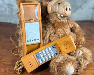 A telephone designed as a plush figure resembling ALF. Features a furry body with an integrated orange telephone handset and functional keypads. Includes a cord for connection.