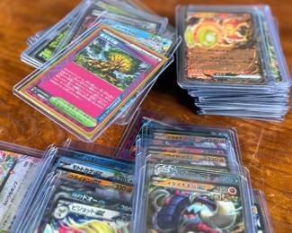 Lot consists of assorted Japanese Pokémon trading cards with holographic and full-art designs. Cards are stored in individual sleeves or protective cases.