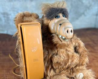 A telephone designed as a plush figure resembling ALF. Features a furry body with an integrated orange telephone handset and functional keypads. Includes a cord for connection.