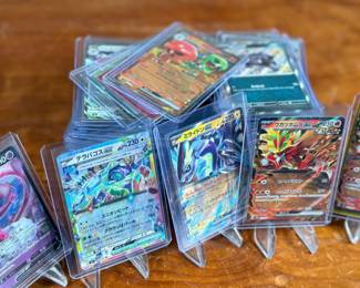 Lot consists of assorted Japanese Pokémon trading cards with holographic and full-art designs. Cards are stored in individual sleeves or protective cases.