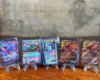 Lot consists of assorted Japanese Pokémon trading cards with holographic and full-art designs. Cards are stored in individual sleeves or protective cases.