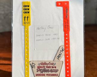 Items from Mötley Crüe’s World Tour (1987-89), including two crew wristbands, one yellow and one red, and a backstage pass patch labeled ‘Working Personnel.’ Mounted on display with handwritten notes documenting their origin.