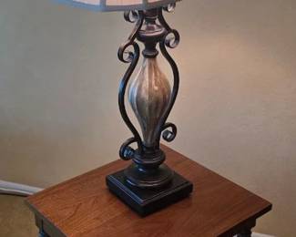 Wrought iron lamp with an iridescent glass column, topped by a cream-colored rectangular shade with rolled edges
