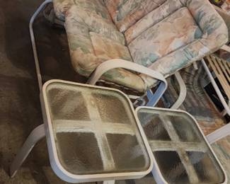 Patio glider loveseat, pair of glass top tables, stack of Rubbermaid outdoor chairs
