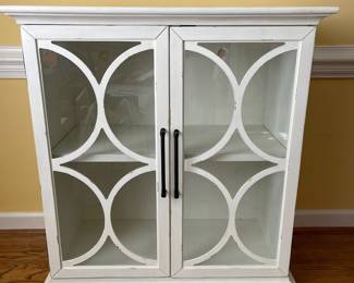 D22 - $350. Haverty’s Edisto accent cabinet. Great condition and solid construction. Distressed white cabinet with glass doors and one shelf. Has a small hole cut in the back to use for electronics. Measures 36” wide  x18” deep x 39” tall. 