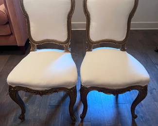 a pair of vintage Louis XV style side chairs featuring ornate, carved wood frames with a gilded finish and white upholstered seats