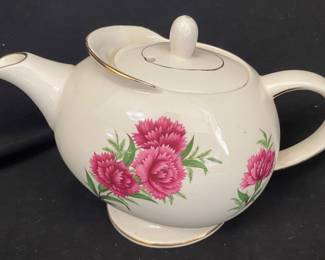 a vintage ceramic teapot decorated with a dark pink carnation pattern and gold trim on the spout, lid, and handle