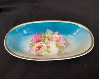a vintage oval porcelain bowl featuring a blue interior, hand-painted pink and yellow roses, and a gold-gilded rim