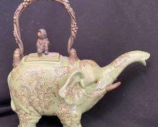  Asian ceramic teapot fashioned in the shape of an elephant, featuring a detailed monkey figurine on the lid and a decorative bronze handle