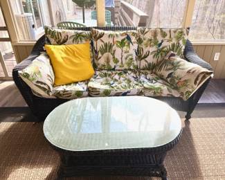 Outdoor wicker seating set including sofa, armchair, ottoman, and glass-top tables, comfortable and ready for the season.