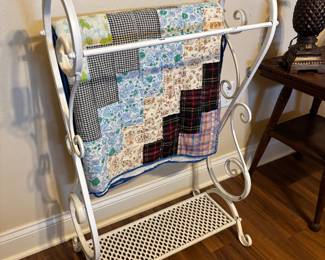 Decorative white wrought iron quilt rack with a mesh bottom shelf