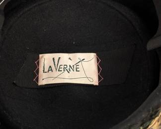Another view of the vintage black velvet pillbox hat with a black green and gold feather trim and a black net veil, label inside reads LaVerne