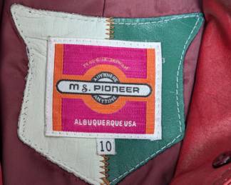 Closeup of the 1970s red leather jacket by Ms Pioneer, featuring a sharp collar, fitted silhouette, and Western-style stitching on the chest; size  10