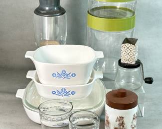 Vintage kitchen ware including a set of vintage CorningWare casserole dishes in the iconic blue cornflower pattern, first introduced in the late 1950s; a vintage Echt Opaline milk glass canister featuring a pastoral "Romantic Rural Town" scene with brown imagery and a brown plastic lid, and a vintage Androck nut chopper or grinder from the 1940s or 1950s