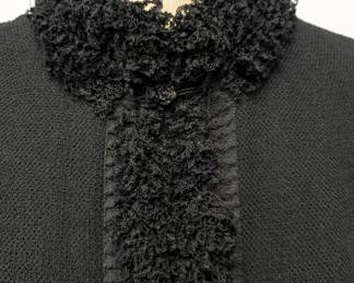 Closeup of the 2003 vintage classic Chanel black boucle wool suit, the jacket and skirt both edged with a looped wool, the jacket closes at the neck with a black camellia flower button; jacket size 42 and skirt size 40.